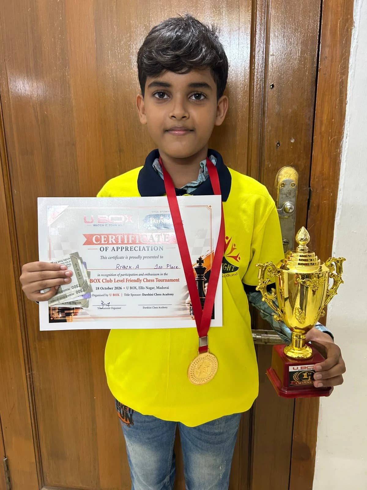 Rithik Amarnath holding the winner's trophy, gold medal and certificate